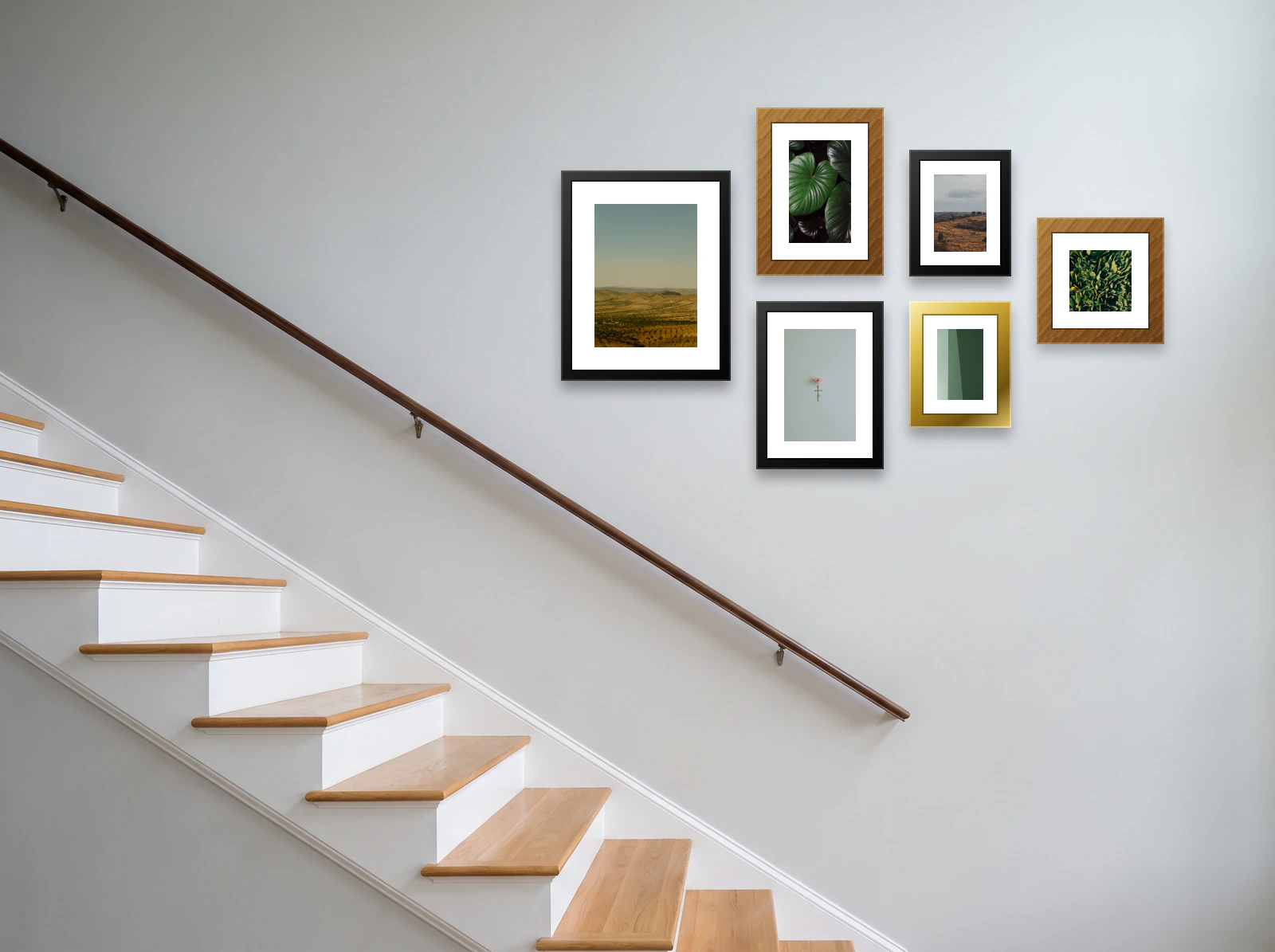 Staircase gallery wall template: a cluster of six frames in four sizes on a pale wall above a white and oak staircase