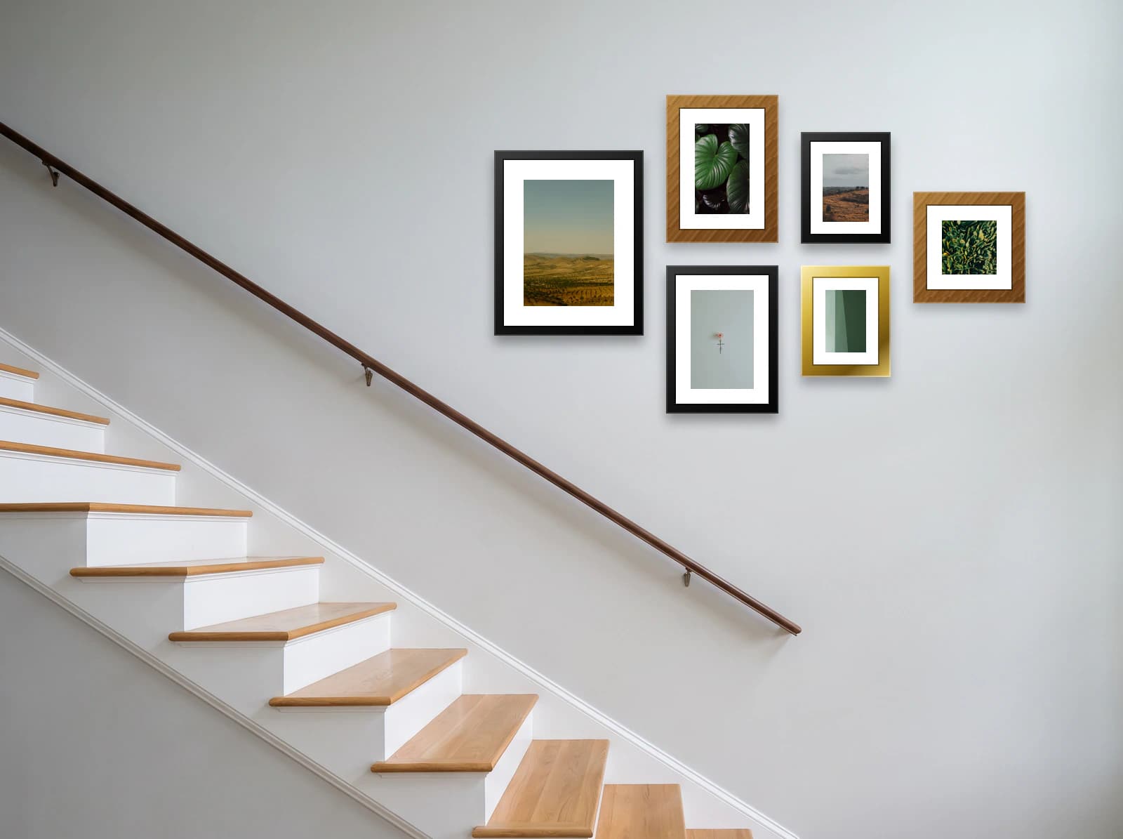 Staircase gallery wall template: a cluster of six frames in four sizes on a pale wall above a white and oak staircase